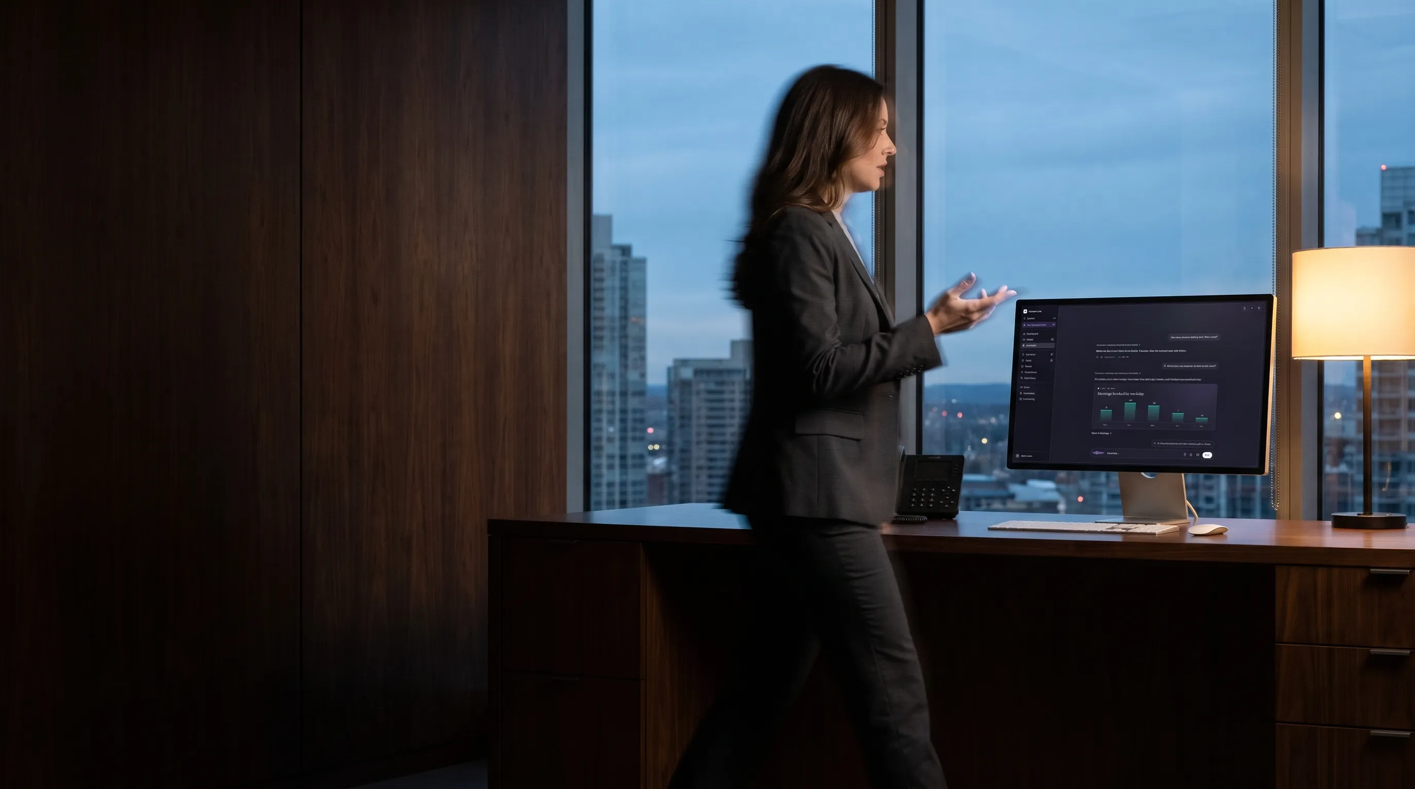 An attorney paces past her desk at dusk, asking a question out loud while the answer appears on her screen.